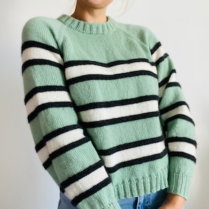 May include: A green and black striped sweater with long sleeves and a crew neck.