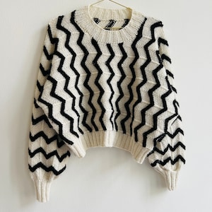 Könnte beinhalten: Ein weißer und schwarzer Pullover mit Chevron-Muster, langen Ärmeln und einem runden Ausschnitt.