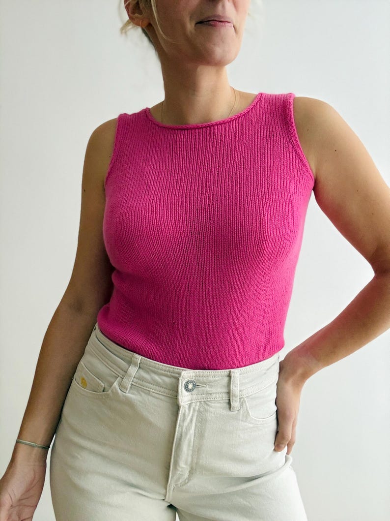 May include: A vibrant pink tank top with a ribbed knit texture. The top has a scoop neckline and is sleeveless. The model is wearing light-colored jeans. The top is a solid color and appears to be made of a soft material.