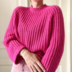 May include: A bright pink ribbed knit jumper with long sleeves and a round neckline.