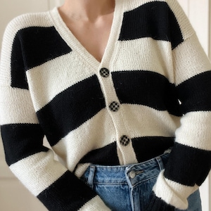 May include: A black and white striped cardigan with a v-neck and button closure. The cardigan is made of a soft, knit fabric.