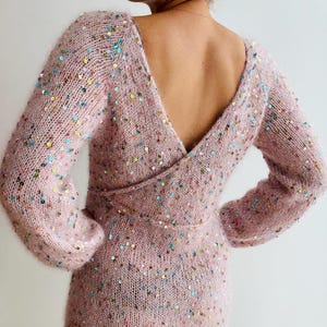 Peut inclure: Robe rose pâle à manches longues, col en V plongeant et taille portefeuille. La robe est ornée de paillettes multicolores. Le dos de la robe est ouvert.