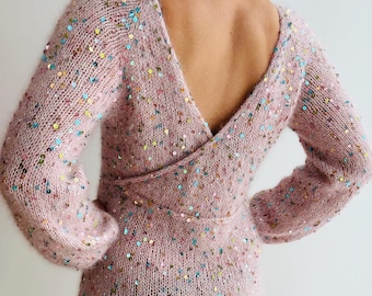 May include: A light pink, long-sleeved dress with a deep V-neck and a wrap-around waist. The dress is covered in colorful sequins. The back of the dress is open, revealing the wearer's back.