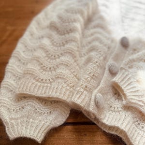 May include: A white crocheted cardigan with a delicate openwork pattern and button closures.