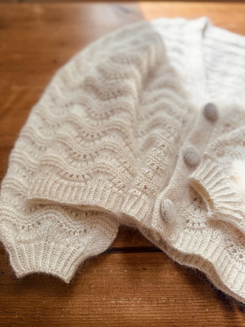 May include: A white crocheted cardigan with a delicate openwork pattern and button closures.