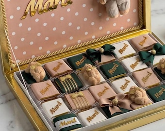 May include: A gold-trimmed gift box with a pink and white polka dot interior lid featuring a plush teddy bear and the gold script text Mard. The box contains an assortment of individually wrapped chocolates decorated with bows and the name Mard.