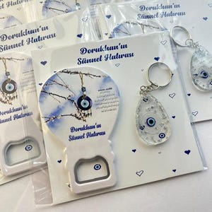 May include: White bottle opener and keychain favors with blue evil eye charms. The bottle opener is shaped like a hot air balloon with the text "Dorukhan'ın Sünnet Hatırası". The keychain has a clear teardrop shape with a blue evil eye.