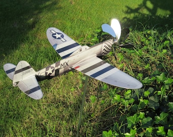 May include: A silver model aeroplane with black and white stripes and a chequered pattern on the tail. The plane has a propeller and is mounted on a metal pole. The plane has the number 22667 and the letters MX on it.