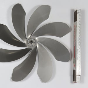 Puede incluir: Un ventilador de metal plateado con ocho aspas, que se asemeja a una flor, con un cubo central y una regla para la escala.