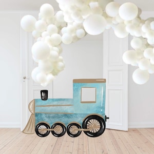 Könnte beinhalten: Ein blauer und brauner Spielzeugzug mit weißen Ballon-Dekorationen im Hintergrund. Der Zug hat einen schwarzen Schornstein und Räder.