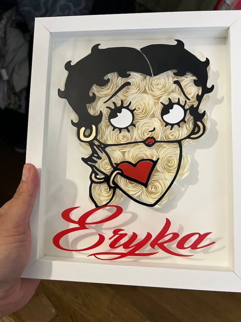 Puede incluir: Un marco blanco con una imagen en blanco y negro de un personaje de dibujos animados con un coraz&oacute;n rojo. El nombre del personaje, "Eryka", est&aacute; escrito en letras rojas cursivas debajo de la imagen.