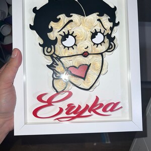 Puede incluir: Un marco blanco con una imagen en blanco y negro de un personaje de dibujos animados con un coraz&oacute;n rojo y el nombre "Eryka" en letras rojas.