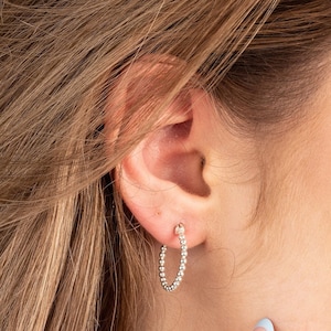 Peut inclure: Boucles d'oreilles créoles en argent avec un design perlé. Les boucles d'oreilles sont petites et délicates.