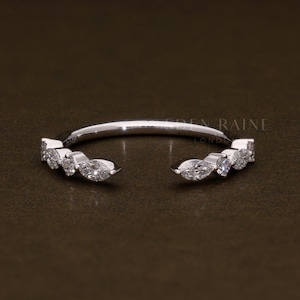 Puede incluir: Un anillo plateado con un diseño abierto, con una serie de pequeñas piedras preciosas con corte marquesa. El anillo tiene un estilo delicado y minimalista, con las piedras preciosas engastadas a lo largo de los bordes exteriores de la banda abierta.