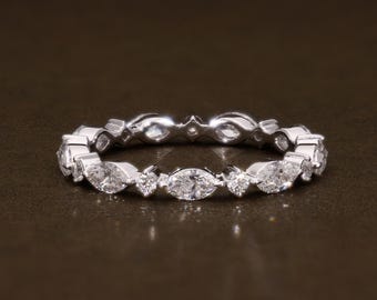 Puede incluir: Un anillo de plata con una banda continua de piedras preciosas transparentes con corte marquesa y redondo. El anillo se encuentra sobre un fondo marrón oscuro, resaltando el brillo de las piedras. Una delicada joya.