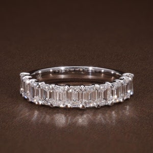 May include: A silver band ring set with a row of rectangular-cut, clear gemstones. The ring is displayed on a brown surface, with the gemstones catching the light. The ring is a piece of jewelry.