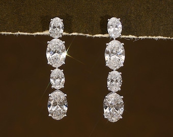 May include: A pair of elegant drop earrings featuring multiple oval-cut diamonds. The diamonds are arranged in a cascading design, with each earring showcasing a series of sparkling stones. The earrings are set against a dark, textured background.