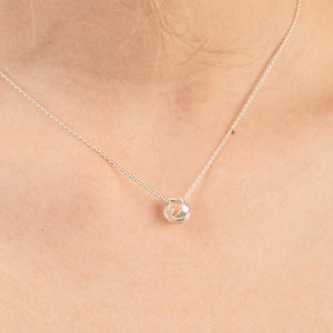 May include: A silver chain necklace with a small, round pendant made of multiple intertwined circles.
