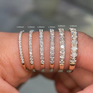 May include: A close-up of six gold band rings, each set with a row of sparkling diamonds. The rings are labeled with their diamond sizes: 1.00mm, 1.20mm, 1.50mm, 1.70mm, 2.00mm, and 2.50mm. The rings are displayed on a finger.
