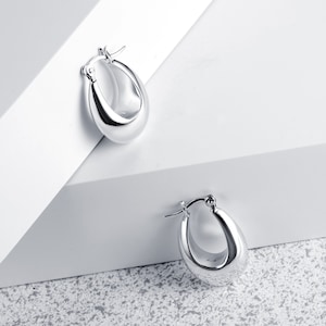 Peut inclure: Une paire de boucles d'oreilles créoles en argent de forme ovale arrondie. Les boucles d'oreilles sont simples et élégantes.