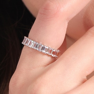 Puede incluir: Un anillo de banda de plata con una fila de piedras transparentes de talla esmeralda.