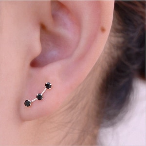 May include: A silver ear cuff with three black gemstones arranged in a curved line. The cuff is worn on the upper lobe of the ear.