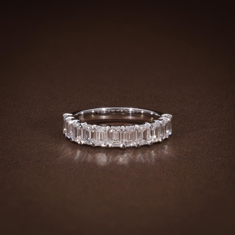 May include: A silver band ring set with a row of rectangular-cut, clear gemstones. The ring is displayed on a brown surface, with the gemstones catching the light. The ring is a piece of jewelry.