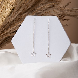May include: A pair of silver star-shaped dangle earrings with a delicate chain.