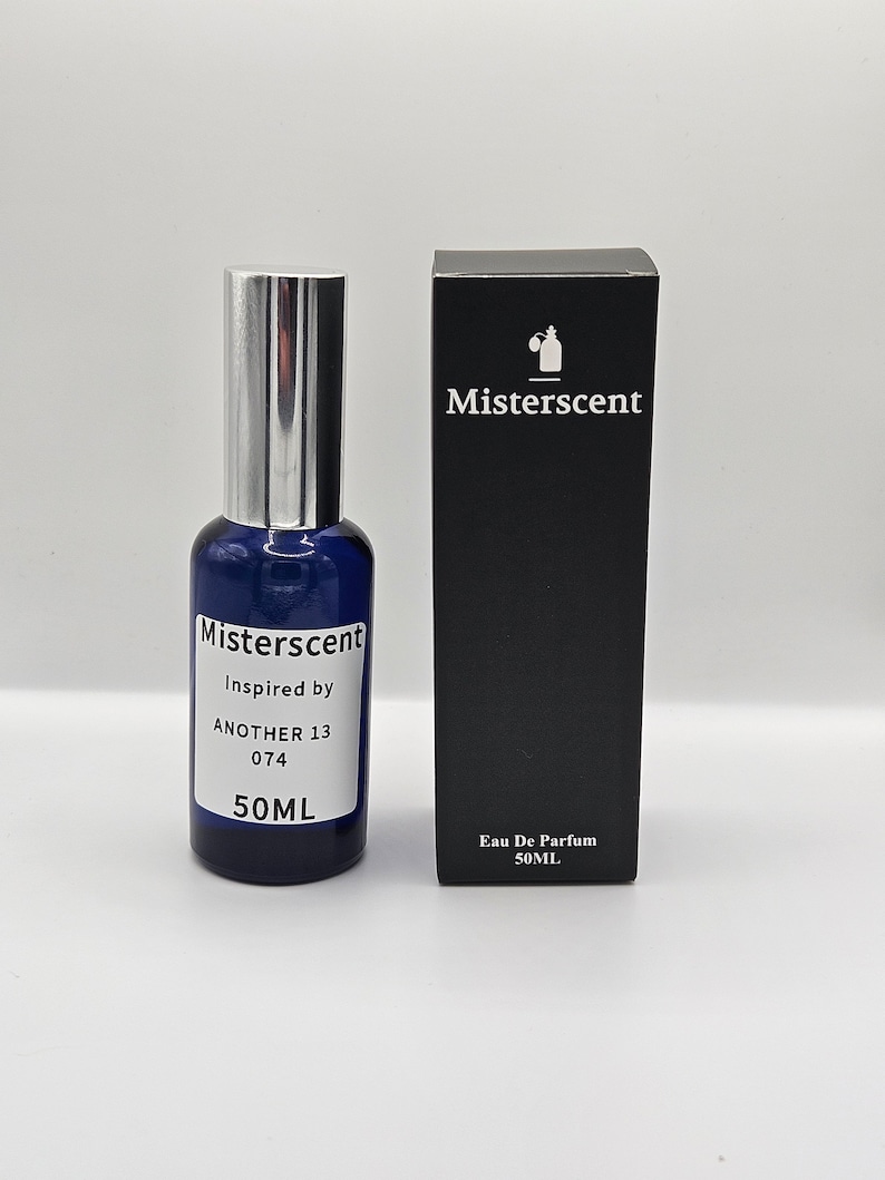 Op de afbeelding: Een blauwe glazen fles MisterScent parfum met een zilveren dop. De fles is gelabeld met de tekst "MisterScent Inspired by ANOTHER 13 074 50ML". De fles staat naast een zwarte doos met de tekst "MisterScent Eau De Parfum 50ML".