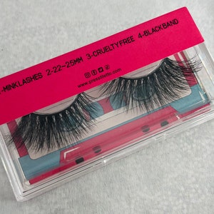 May include: A clear plastic case with a pink lid containing a pair of black mink eyelashes. The lid has the text "1-MINK LASHES 22-22-25MM 3-CRUELTY FREE 4-BLACK BAND" and the website address "www.pressliletto.com".