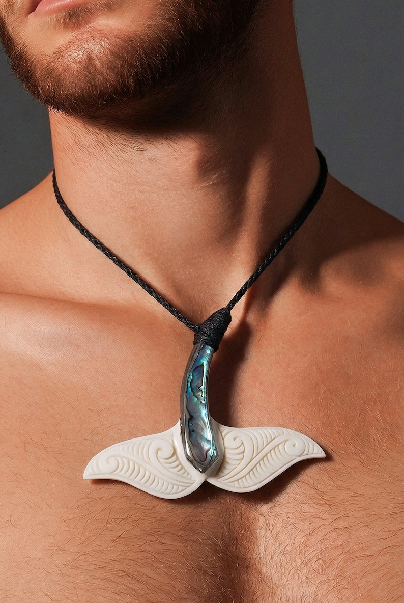 May include: A pendant necklace featuring a whale tail design. The pendant has a white, carved tail with a curved, iridescent abalone shell accent. The necklace has a black, braided cord.
