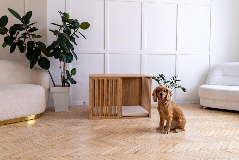 May include: A rectangular wooden dog crate with vertical slats on the front and side panels, featuring a light wood finish and a flat top surface. Inside the crate, a light-colored cushioned mat is visible on the floor of the enclosure.