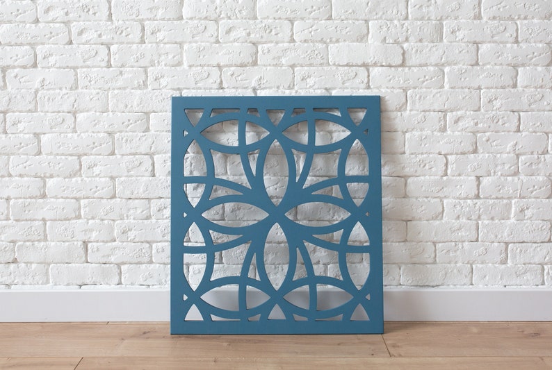K&ouml;nnte beinhalten: Eine tealblaue dekorative Wandverkleidung mit einem geometrischen Muster aus &uuml;berlappenden Kreisen und Ovalen. Die Verkleidung ist aus Holz und hat ein ausgeschnittenes Design.