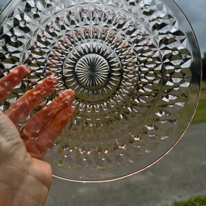 Op de afbeelding: Een heldere glazen plaat met een diamantpatroon. De plaat heeft een verhoogd midden met een stervormig ontwerp.