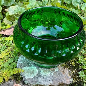 May include: A large, deep green glass bowl with a textured, fluted design. The bowl is sitting on a rock covered in moss.