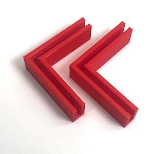 May include: Two red plastic corner brackets, stacked on top of each other. The brackets are designed to be used as a corner support for a shelf or other structure.