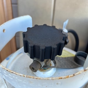 May include: Close-up of a black plastic valve knob with a starburst design on top of a propane tank.