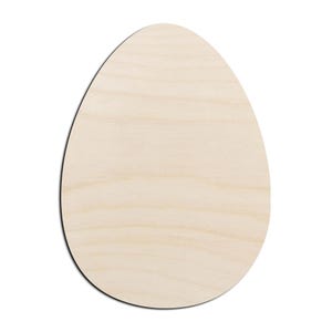 May include: A flat, egg-shaped cutout made of light-colored, unfinished wood. The surface displays a natural wood grain pattern with horizontal lines running across the smooth, pale beige texture of the oval-shaped wooden craft piece.