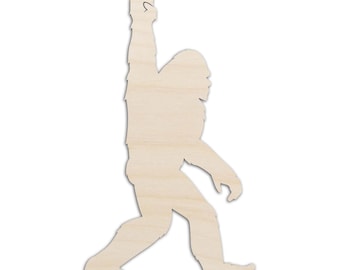 May include: A light-colored, flat wooden cutout in the shape of a Bigfoot or Sasquatch figure. The creature is depicted in profile, walking forward with one arm raised high, displaying a peace sign gesture with its fingers extended upward.