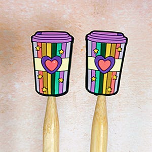 May include: Two colorful rainbow striped coffee cups with a pink heart on each. The cups are attached to wooden knitting needles.
