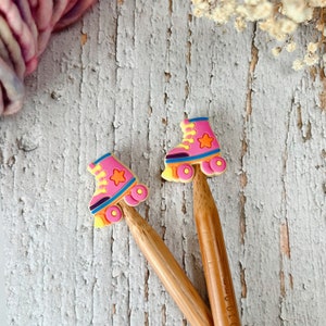 May include: Two wooden knitting needles with pink and yellow roller skate stitch markers. The roller skates have a star on the side.