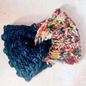 May include: A colorful knitted headband with a navy blue crocheted section. The headband has a small leather tag with the text "The Blue" on it.