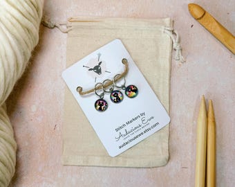 May include: Set of three colorful stitch markers with a cat design. The markers are on a white card with the text "Stitch Markers by Audacious Ewe" and a website address.