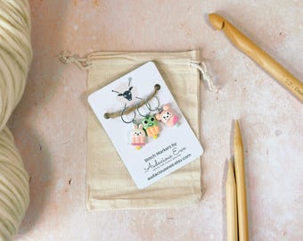 May include: A set of three colorful stitch markers featuring a frog, a bunny, and a pig. The markers are shaped like popsicles and have a white background with the text "Stitch Markers by Audacious Eve" and a website address.