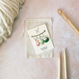 May include: Set of three colorful stitch markers in a small white drawstring bag. The markers are shaped like ice cream cones, a cup of coffee, and a watermelon slice. The bag has a tag that reads "Stitch Markers by Isle Stitch".