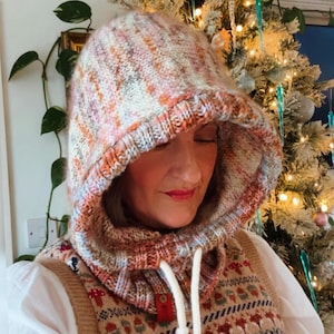 May include: A knitted hood in a mix of colors including orange, pink, and cream. The hood has a drawstring and a ribbed edge. The hood is part of a cowl neck warmer. The cowl neck warmer has a red tag attached to it.