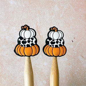 May include: Two decorative pumpkin-shaped toppers. Each topper is stacked with three layers: an orange pumpkin base, a black and white cow-print layer, and a white pumpkin top. The toppers are on wooden sticks, perfect for Halloween or fall-themed crafts.