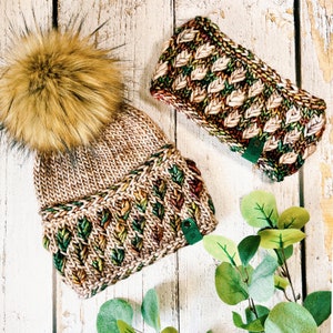 Könnte beinhalten: Eine braune und grüne Strickmütze mit einem flauschigen Bommel oben. Die Mütze hat ein Blatt-Muster und ein braunes Leder-Etikett.