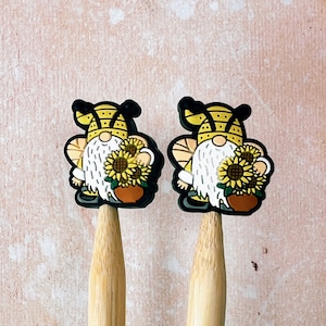 May include: Two yellow and black gnome-shaped kitchen utensil holders with sunflowers. The holders are made of silicone and have a wooden handle.