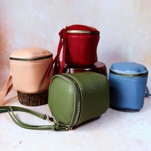 May include: Four small, square-shaped zippered pouches in various colors: light pink, red, green, and blue. Each pouch has a textured surface and a contrasting zipper. The green pouch has a long strap with a gold-colored clasp.